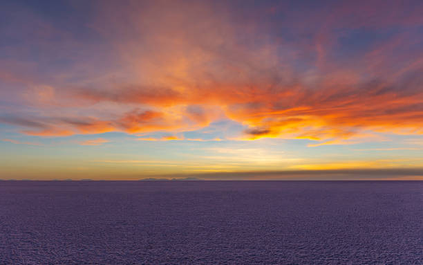 A salt lake reflects the colors of sunrise, with volcanoes on the horizon